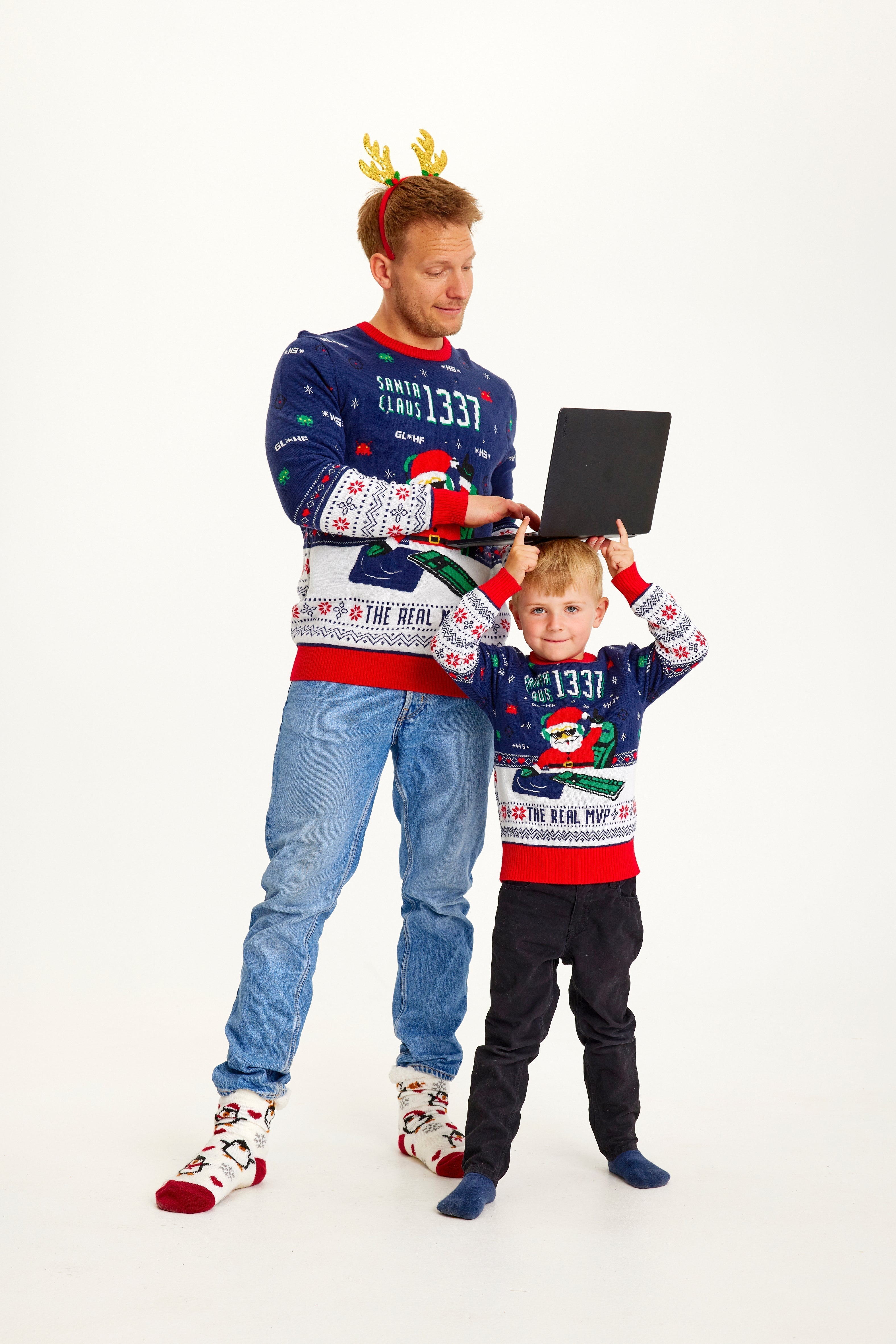 Un homme posant et un enfant portant un pull de Noël bleu et rouge avec un Père Noël et des lumières.